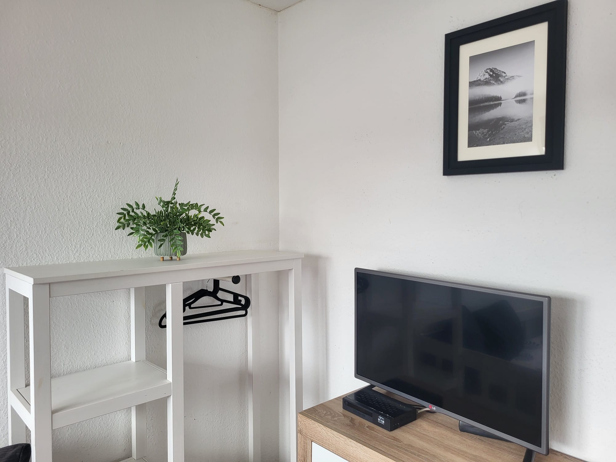 Wohnbereich im Miniapartment mit Fernseher, Ablagetisch und Kleiderbügeln